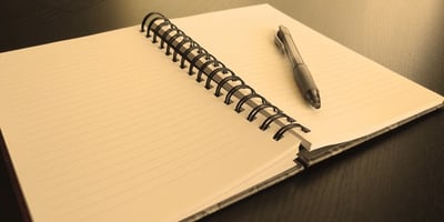 Open wire-bound notebook showing empty pages and a pen